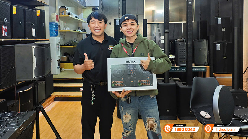 Nhân viên bán hàng và khách tại cửa hàng HDRadio, tay cầm hộp DJ DDJ-FLX2, nền là các thiết bị âm thanh